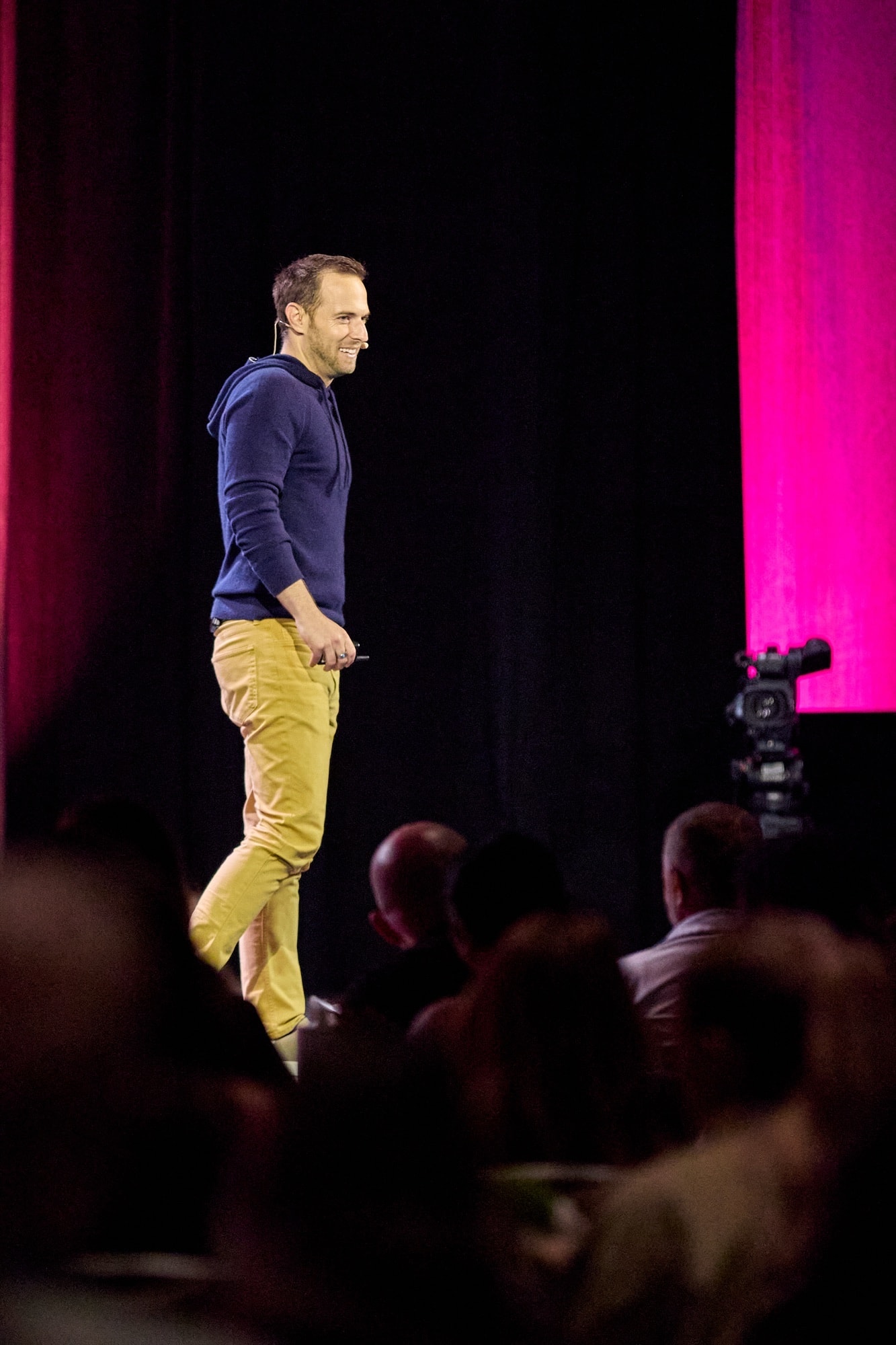 Speaker on stage with dramatic backlit drapes — sample event coverage frame